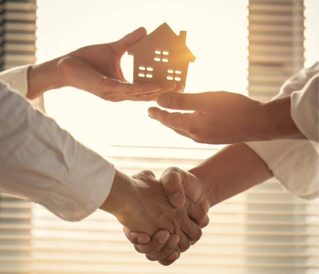 Two people shaking hands over a house deal